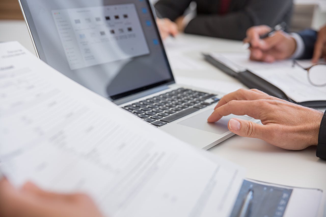 Close-up of hands working on documents and a laptop in an office setting, illustrating teamwork and productivity.